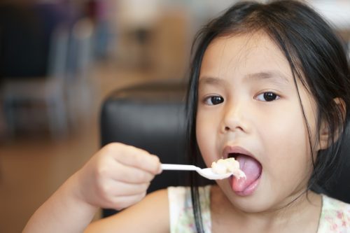 Cute young Asian girl eating tuna salad and corn 