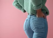 Close-up rear view of a woman wearing jeans and a green sweater on a pink background