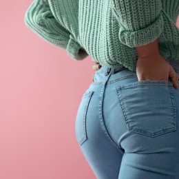 Close-up rear view of a woman wearing jeans and a green sweater on a pink background