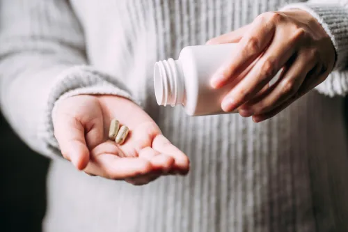 A closeup of someone taking two vitamin capsules into their palm from a white bottle