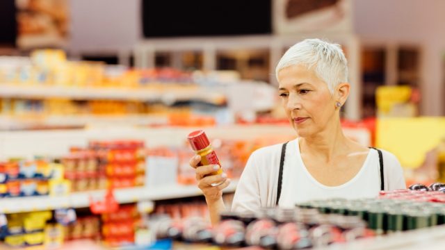Mature smiling woman shopping in local supermarket. Standing by produce stand and choosing spices. Reading nutrition label.