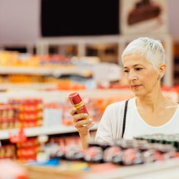 Mature smiling woman shopping in local supermarket. Standing by produce stand and choosing spices. Reading nutrition label.