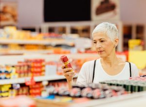 Mature smiling woman shopping in local supermarket. Standing by produce stand and choosing spices. Reading nutrition label.