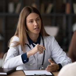 Female doctor therapist in white uniform with stethoscope consulting woman patient at meeting, sitting at desk in hospital, giving recommendations, explaining medical checkup results at appointment