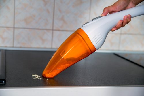 The female hand holds a portable vacuum cleaner, cleaning up crumbs on the counter