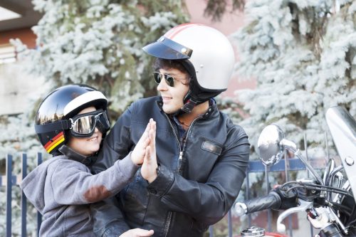 father and son motorcyclists giving each other a high five