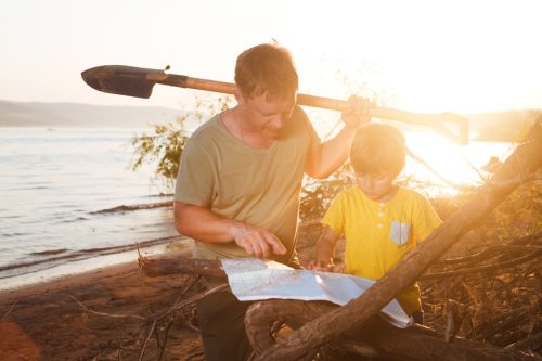 father and son look at a treasure map together during sunset