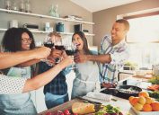Group of young cheerful friends toasting with wine glasses while cooking in kitchen.