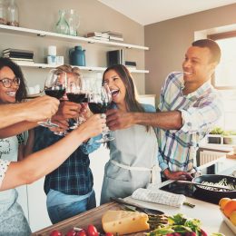 Group of young cheerful friends toasting with wine glasses while cooking in kitchen.