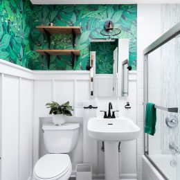 A bright white bathroom with a beautiful, colorful green leaf wallpaper.