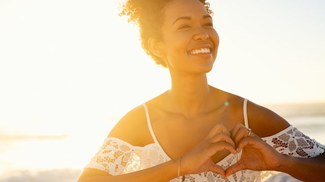 Smiling woman making heart shape shape with hands at sunrise
