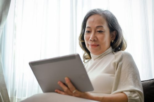older asian woman using tablet on her couch 