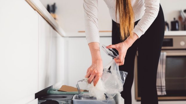 Unrecognizable woman throwing waste away in her kitchen bins, woman recycling waste, separating plastic from paper and organic waste. Woman hand putting waste in her recycling kitchen drawer.