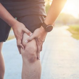 man use hands hold on his knee while running on road in the park.