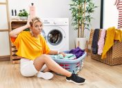 Young caucasian woman putting dirty laundry into washing machine confuse and wondering about question. uncertain with doubt, thinking with hand on head