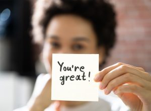 woman holding up a post-it note saying "you're great"