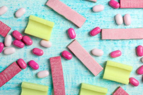 yellow and pink chewing gum with small candies on a blue wooden background