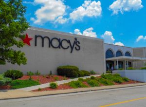 landscaping near entrance to retailer with corporate sign with star logo hanging on outside wall. Cincinnati based Macy’s department stores operates over 660 locations in the United States and is a common anchor tenant at many suburban malls.