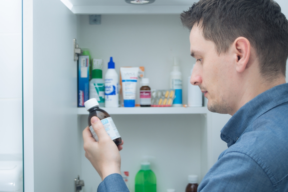 A man looking at a bottle he has just taken from his medicine cabinet