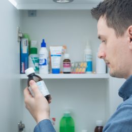 A man looking at a bottle he has just taken from his medicine cabinet