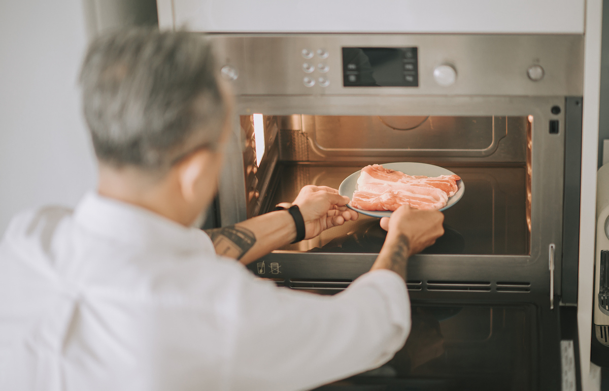 Man putting a plate of raw bacon in the microwave
