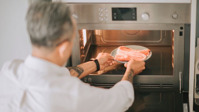 Man putting a plate of raw bacon in the microwave