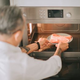 Man putting a plate of raw bacon in the microwave