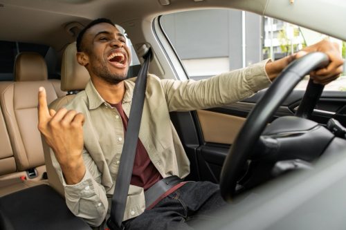 Joyful black man dancing in car, singing while driving his car.