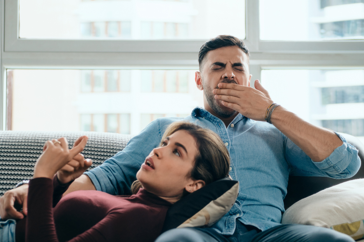 Bored man yawning while woman keeps talking. Young couple having boring conversation at home.