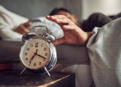 Ảnh chụp một thanh niên với lấy đồng hồ báo thức sau khi thức dậy trên giường ở nhà