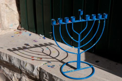 A blue, metal Hanukkah menora casts a shadow on a stone wall outside