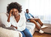 Unhappy Couple After an Argument in the Living Room at Home. Sad Pensive Young Girl Thinking of Relationships Problems Sitting on Sofa With Offended Boyfriend, Conflicts in Marriage,