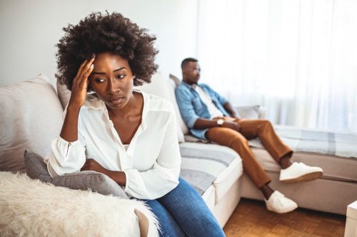 Unhappy Couple After an Argument in the Living Room at Home. Sad Pensive Young Girl Thinking of Relationships Problems Sitting on Sofa With Offended Boyfriend, Conflicts in Marriage,
