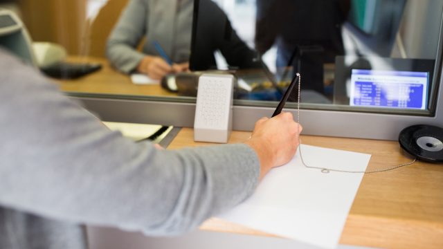A person signs a document at a counter in a bank.