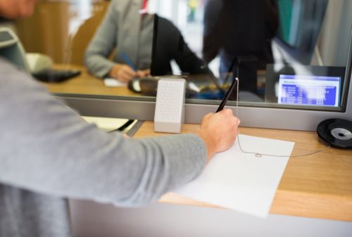 A person signs a document at a counter in a bank.