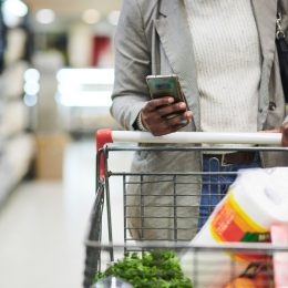 woman, hands and phone with trolley for shopping, checklist or ecommerce at the mall.