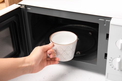 Woman with cup of water near microwave oven in kitchen, closeup