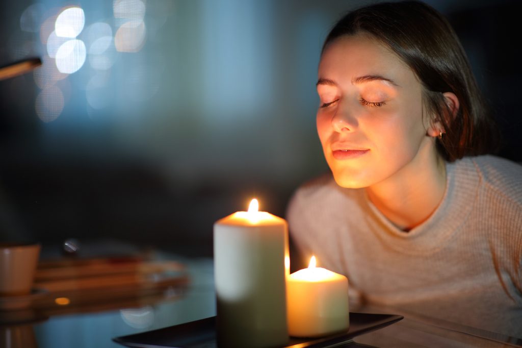 Relaxed woman smelling a lighted scented candle in the night at home