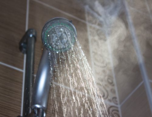 Low angle view of flowing shower head in the bathroom. Horizontal composition. Image taken indoors and developed from Raw format. Focus on water. Shower head and other background are blurred.