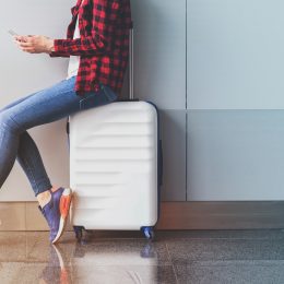 Woman sitting on white suitcase texting