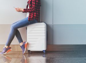 Woman sitting on white suitcase texting