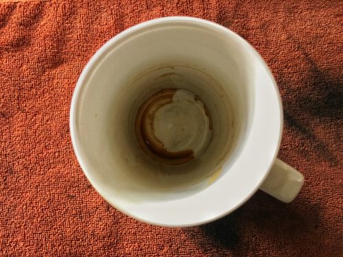 Empty white mug with coffee stain on an orange background