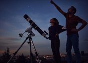 A father and daughter stargazing at dusk while using a telescope