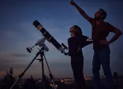 A father and daughter stargazing at dusk while using a telescope