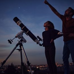 A father and daughter stargazing at dusk while using a telescope
