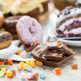 junk food, sweets and unhealthy eating concept - close up of chocolate pieces, jelly beans, glazed donuts and cake on wooden table