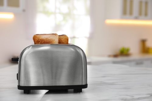 Modern toaster with slices of bread on table in kitchen. Space for text