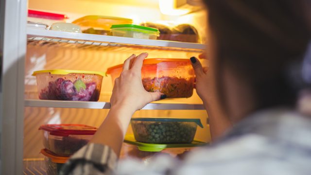 A person grabbing food from a fridge filled with Tupperware containers with leftovers