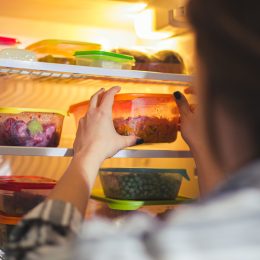 A person grabbing food from a fridge filled with Tupperware containers with leftovers