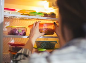 A person grabbing food from a fridge filled with Tupperware containers with leftovers